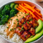 Overhead shot of a spicy chicken bowl with rice, sliced avocado, bell peppers, and sesame seeds.