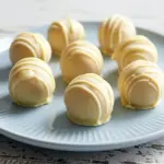 A plate of creamy, no-bake lemon truffles coated in white chocolate and sprinkled with lemon zest — a bright, zesty treat perfect for Gourmet Snack Ideas, Light And Healthy Desserts, and Healthy Easy Sweets.