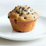 A batch of High Protein Snacks Low Sugar Healthy Muffins Chocolate Chip baked golden brown, made with oats, Greek yogurt, and Muffins Made With Protein Powder, cooling on a wire rack with melty chocolate chips on top.