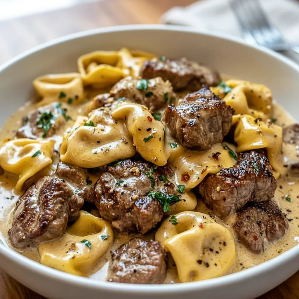 Close-up of seared Garlic Steak and cheesy Tortellini coated in creamy sauce, steaming in a cast-iron Skillet — ideal for cozy Weeknight Meals.