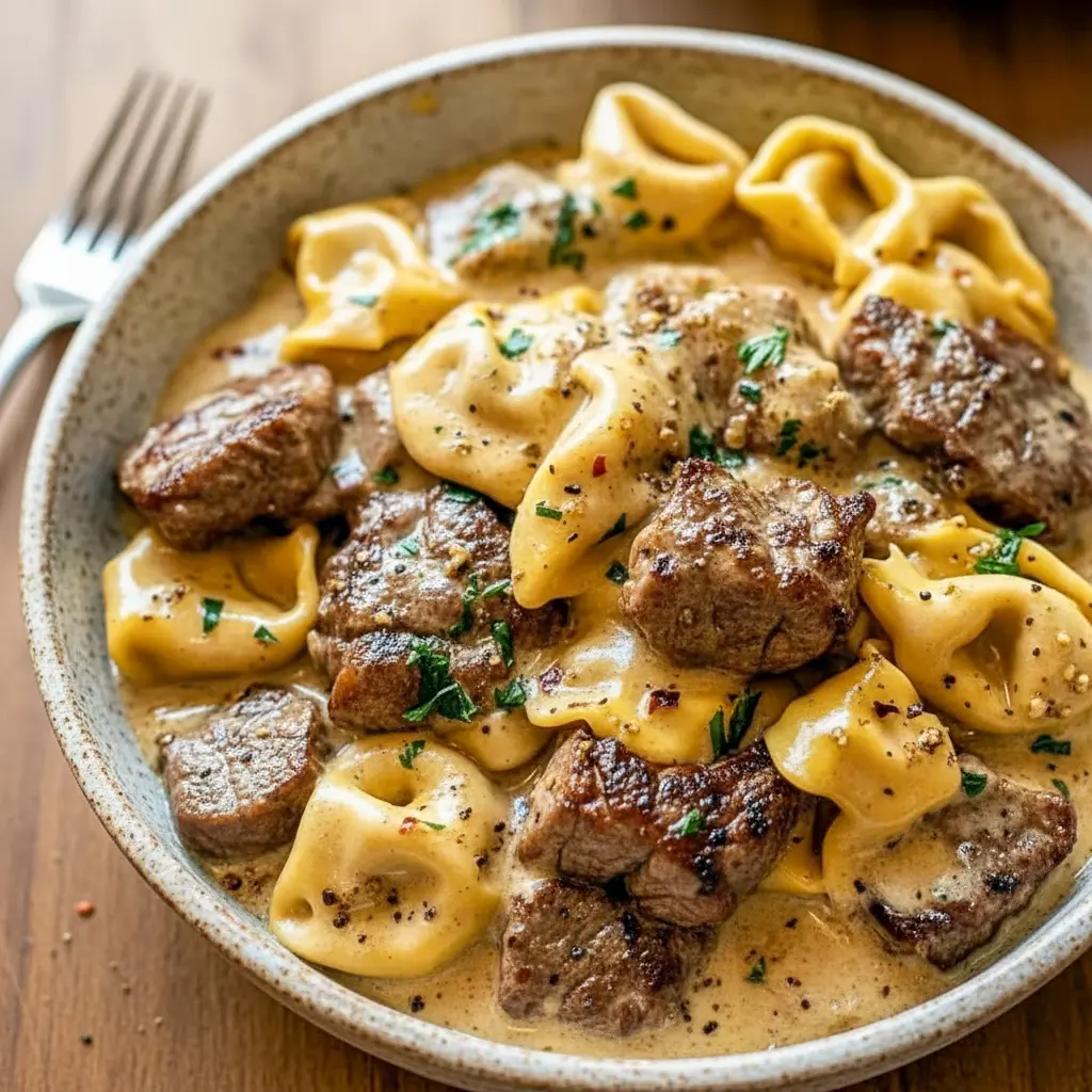 Close-up of seared Garlic Steak and cheesy Tortellini coated in creamy sauce, steaming in a cast-iron Skillet — ideal for cozy Weeknight Meals.