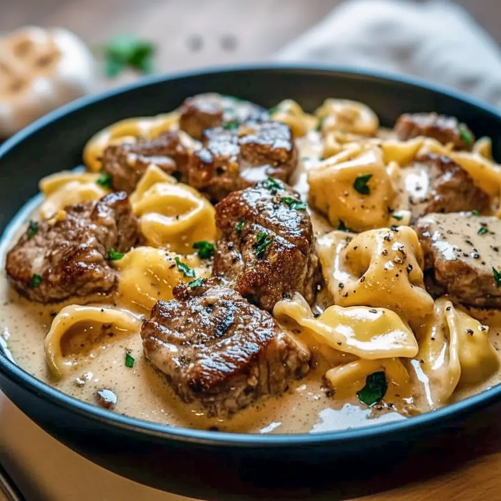 Close-up of seared Garlic Steak and cheesy Tortellini coated in creamy sauce, steaming in a cast-iron Skillet — ideal for cozy Weeknight Meals.