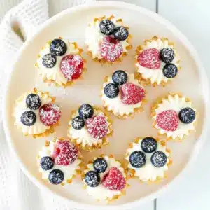 No-Bake Cheesecake Bites — close-up of mini fillo cups filled with creamy cheesecake, topped with raspberries and blueberries, arranged on a serving platter.