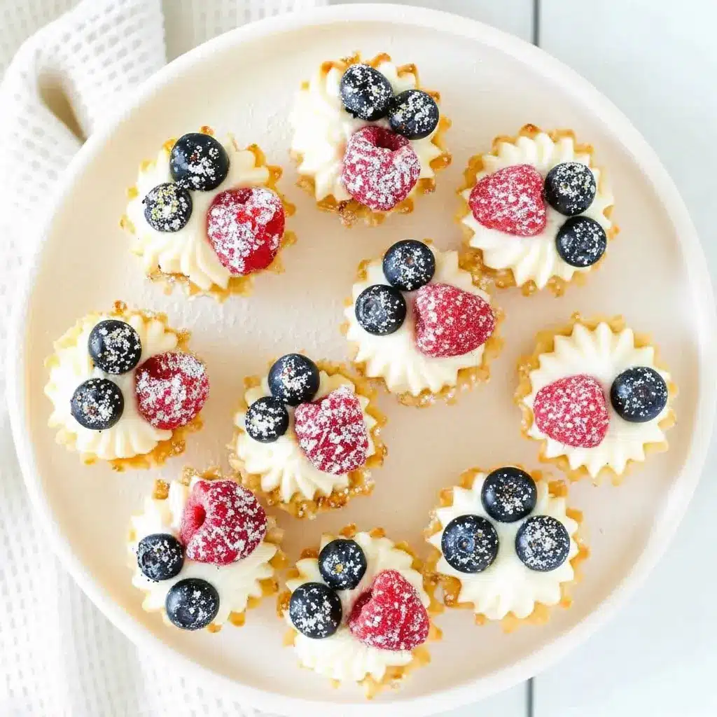 No-Bake Cheesecake Bites — close-up of mini fillo cups filled with creamy cheesecake, topped with raspberries and blueberries, arranged on a serving platter.
