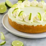 Key Lime Cheesecake slice on a white plate, topped with whipped cream and lime zest — close-up of the smooth, tangy filling.