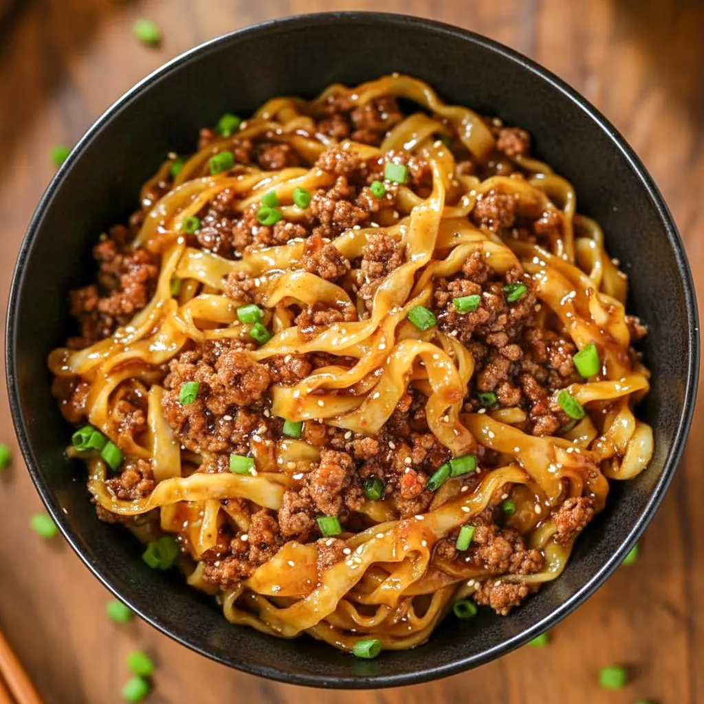 Skillet of glossy Potsticker Noodle Bowl with ground pork, wide noodles, and bright cabbage slaw, garnished with green onions—an inviting example of quick Potsticker Noodles.