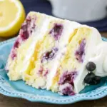 Lemon Blueberry Cake — three-layer lemon cake sliced to reveal blueberry-studded crumb and lemon curd filling, topped with lemon mascarpone frosting and fresh berries.