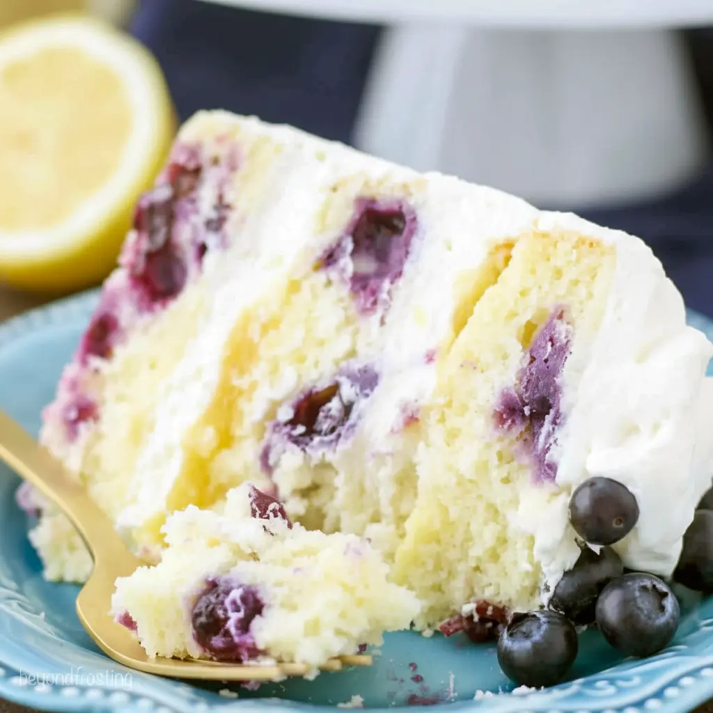 Lemon Blueberry Cake — three-layer lemon cake sliced to reveal blueberry-studded crumb and lemon curd filling, topped with lemon mascarpone frosting and fresh berries.
