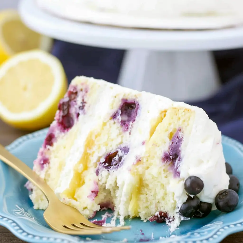 Lemon Blueberry Cake — three-layer lemon cake sliced to reveal blueberry-studded crumb and lemon curd filling, topped with lemon mascarpone frosting and fresh berries.