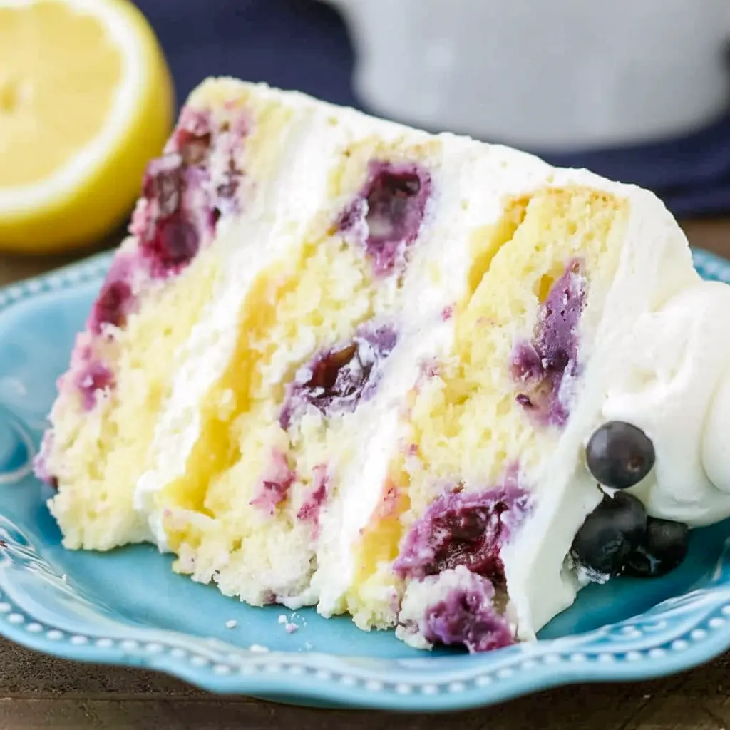 Lemon Blueberry Cake — three-layer lemon cake sliced to reveal blueberry-studded crumb and lemon curd filling, topped with lemon mascarpone frosting and fresh berries.