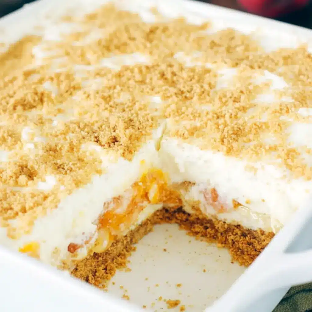 Close-up of No-Bake Peach Yum Yum in a glass dish: golden graham crust, fluffy cream-cheese layers, glossy peach pie filling, and a light sprinkle of crumbs.