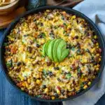 Overhead shot of a Taco Rice Skillet in a cast-iron pan topped with sliced avocado, cilantro, and crushed tortilla chips.