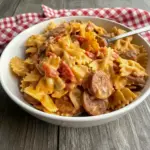 Easy Smoked Sausage Pasta — one-pot creamy Cajun bowtie pasta with browned smoked sausage rounds, diced tomatoes with chiles, and gooey cheddar in a skillet.