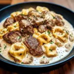 Garlic Steak bites and cheesy Tortellini in a creamy sauce in a hot Skillet, garnished with parsley.