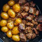 Close-up of Easy Crockpot Dinner: glossy garlic-butter beef bites and golden halved potatoes on a plate, sprinkled with parsley.