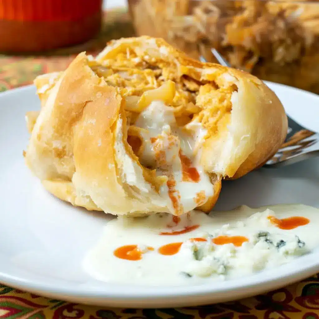 Buffalo Chicken Bombs on a serving platter: golden-brown biscuit bombs split open to reveal spicy shredded chicken and melted cheese, with a bowl of blue cheese dressing and hot sauce beside them.