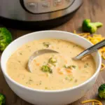 A bowl of Instant Pot Broccoli Cheddar Soup topped with melted cheese, showing a creamy Instant Pot Broccoli Soup with broccoli and carrots.
