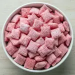 Bowl of Strawberry Shortcake Puppy Chow: white-chocolate coated cereal dusted with powdered sugar and crushed freeze-dried strawberries, a colorful Snack Mix for parties.