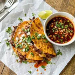 Crock Pot Birria Tacos served with a rich dipping bowl, styled as one of the best Birria Tacos Crockpot dinners for taco night.
